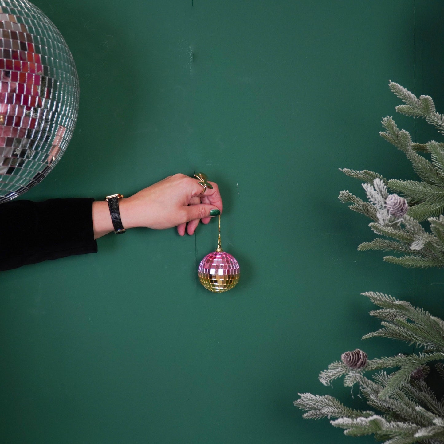 Discokugel „für gute Laune“ von House Vitamin (6 cm) in Rosa-Gold, gehalten vor grünem Hintergrund mit Tannenzweigen und großer silberner Discokugel – funkelnder Hingucker als Weihnachtsdeko oder Geschenkidee