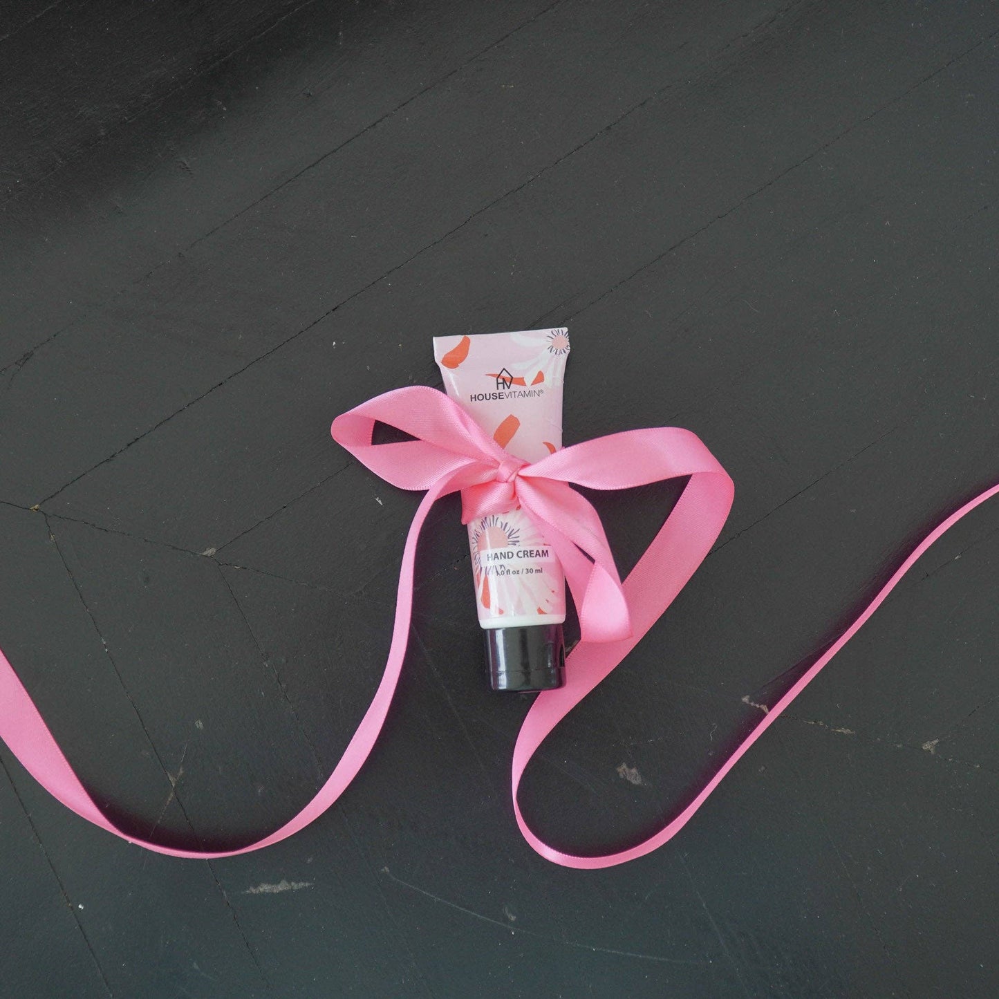 Kleine Tube Handcreme „Pfingstrosenblüte" von House Vitamin, 30 ml, mit rosa Geschenkschleife auf dunklem Holzuntergrund – pflegende Handpflege und liebevolle Geschenkidee