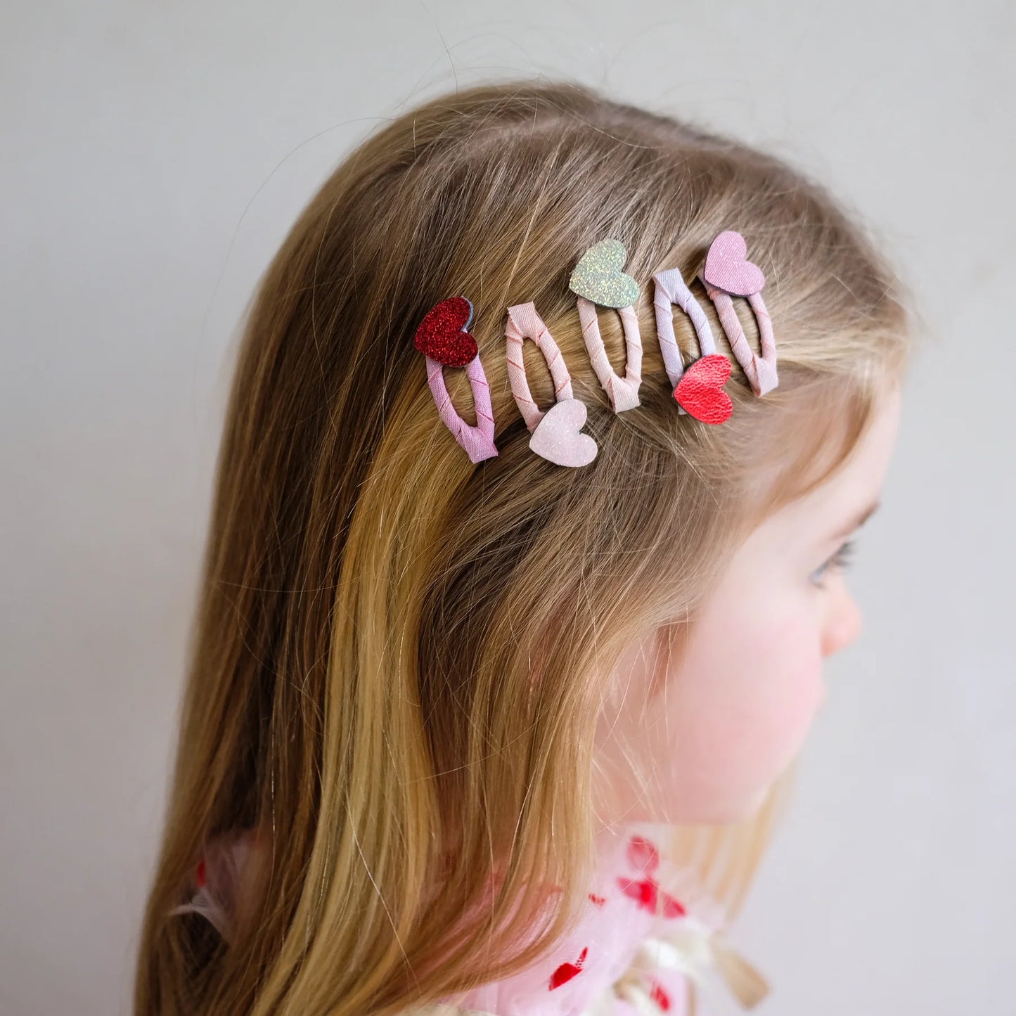 Haarspangen mit Herz-Motiven von Mimi & Lula, 5er Set in Rosa-, Rot- und Goldtönen mit Glitzer, getragen im Haar eines Kindes – kinderfreundlicher Haarschmuck und liebevolle Geschenkidee