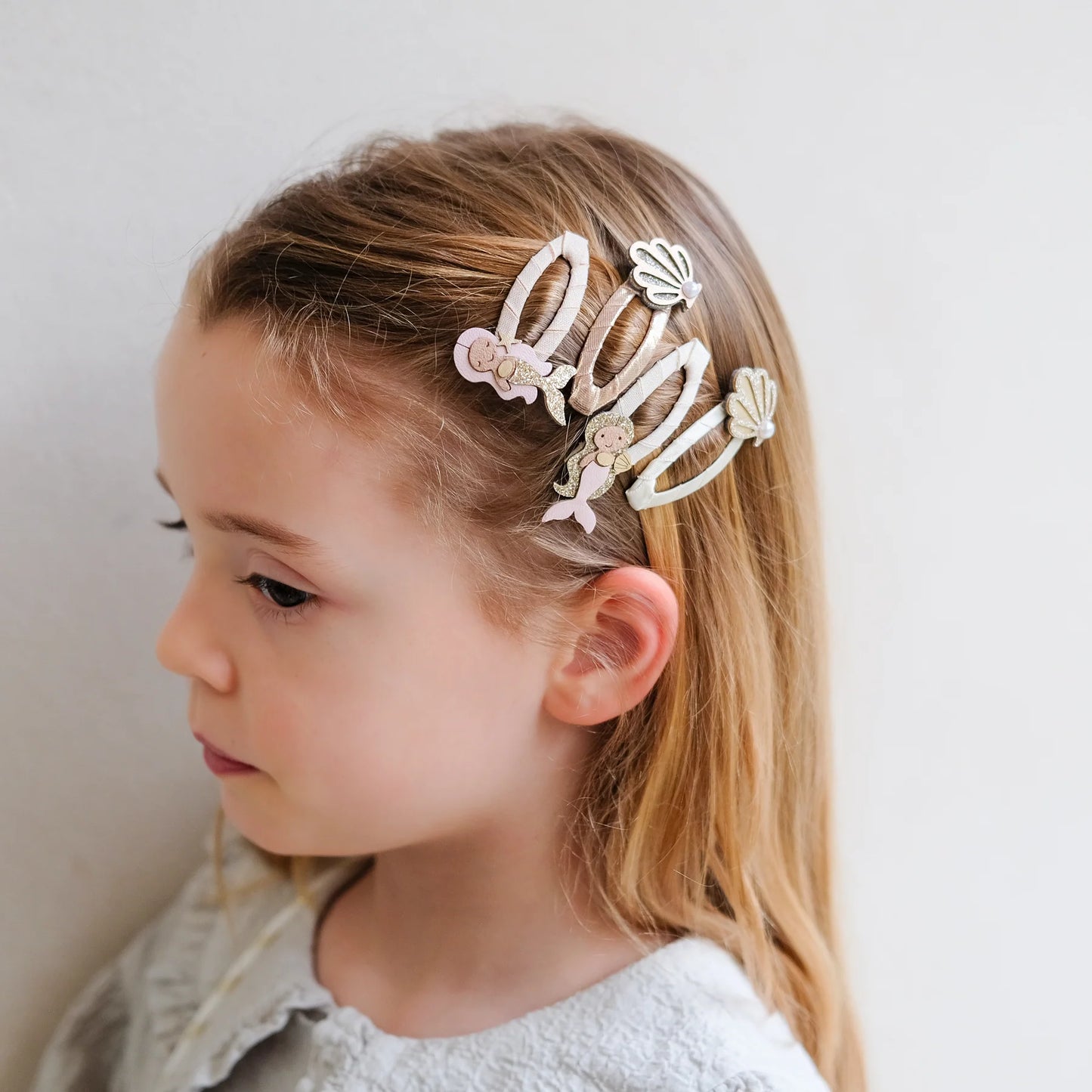 Haarspangen mit Meerjungfrauen-Motiv von Mimi & Lula, 4er Set in Rosa-, Creme- und Goldtönen mit Meerjungfrauen- und Muschelmotiven, getragen im Haar eines Kindes – kinderfreundlicher Haarschmuck und liebevolle Geschenkidee