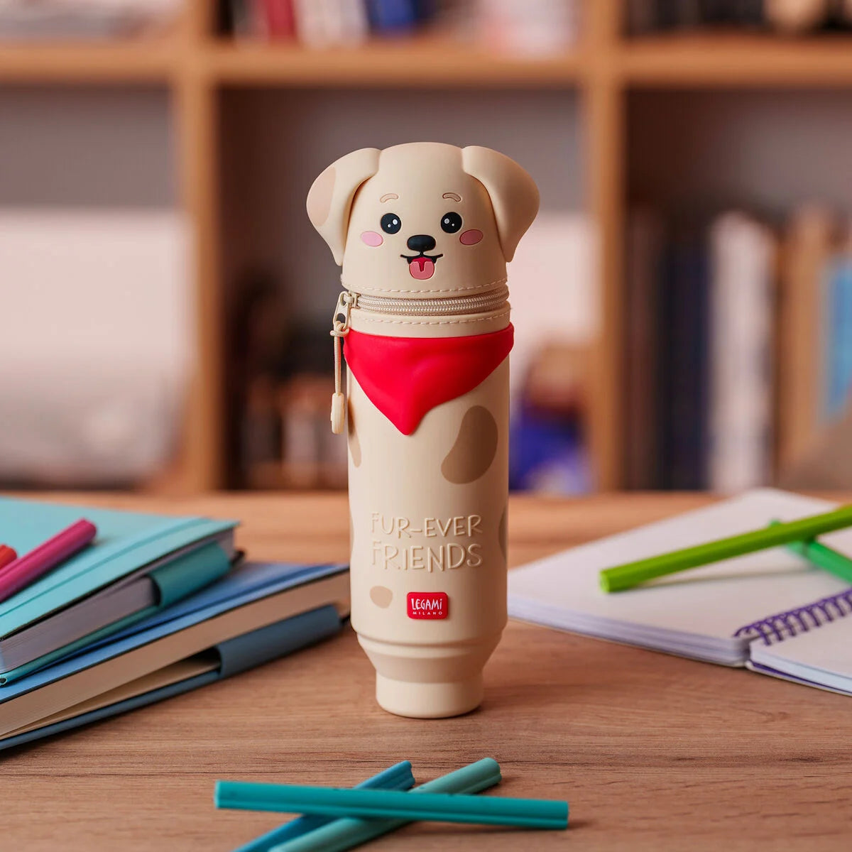 Kawaii Federmäppchen Golden Hunde-Motiv Fur-Ever Friends von Legami limitiert geschlossen aufrecht stehend auf Holztisch mit Buechern und Stiften beige Hunden-Form mit rotem Halstuch und Fur-Ever Friends Schriftzug Buecherregal im Hintergrund