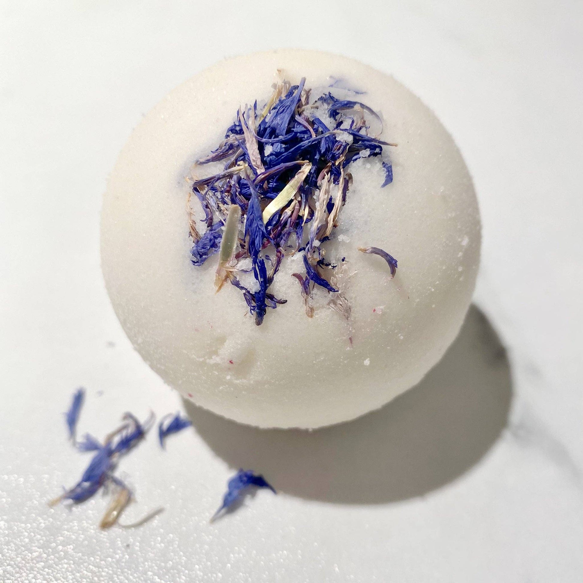 Nahaufnahme der handgefertigten Badekugel „Kornblume" mit getrockneten blauen Kornblumenblüten, gepflegt mit Bio-Sheabutter und Mandelöl, sorgt für ein entspannendes Spa-Erlebnis für Zuhause