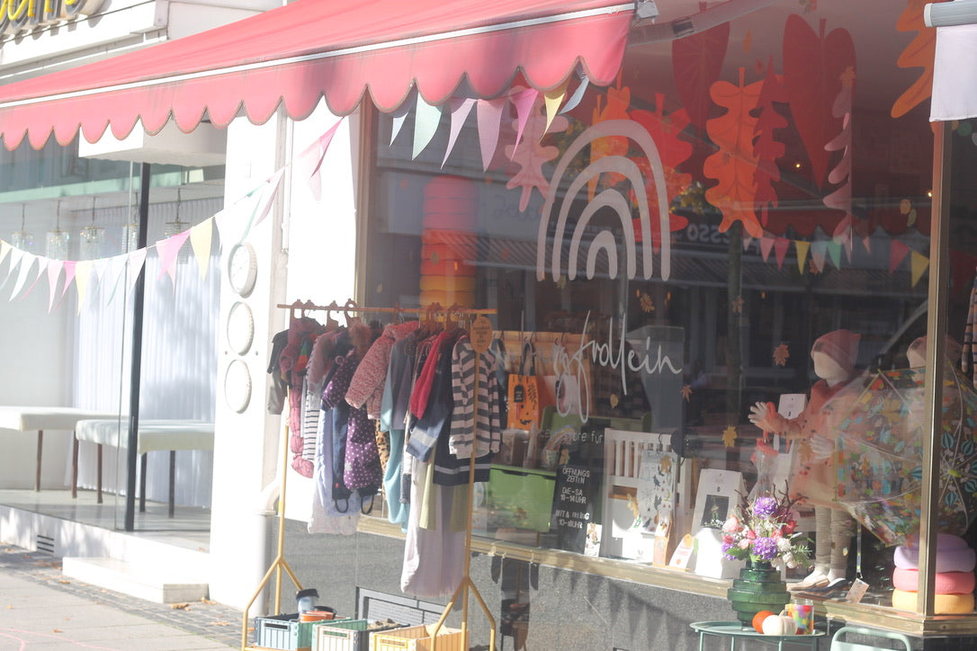 Außenansicht des Burgfrollein Concept Stores für Klein & Groß mit Schaufenster, roter Markise und Wimpelkette