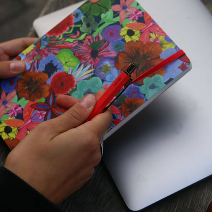 Cedon Kugelschreiber in Rot matt – in der Hand gehalten vor einem bunten Notizbuch mit Blumenmotiv