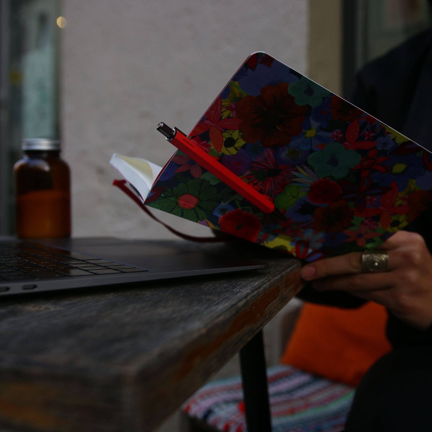Roter Kugelschreiber von Cedon befestigt an einem Notizbuch mit Blumenmotiv im stimmungsvollen Lifestyle-Look am Arbeitsplatz bei Burgfrollein