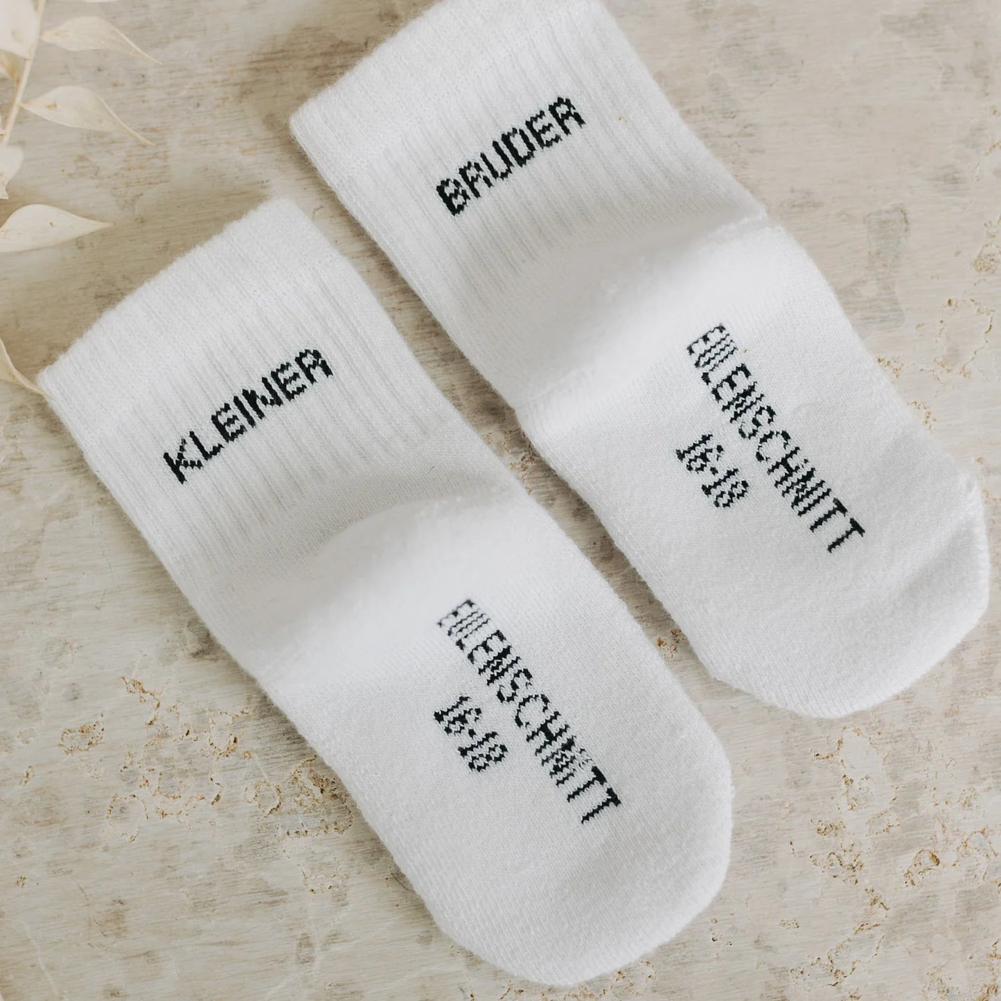 Eulenschnitt Baby-Socken „Kleiner Bruder" in Weiß, Größe 16-18, Produktaufnahme mit sichtbarem Eulenschnitt Schriftzug auf der Sohle bei Burgfrollein