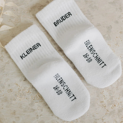 Eulenschnitt Baby-Socken „Kleiner Bruder" in Weiß, Größe 16-18, Produktaufnahme mit sichtbarem Eulenschnitt Schriftzug auf der Sohle bei Burgfrollein