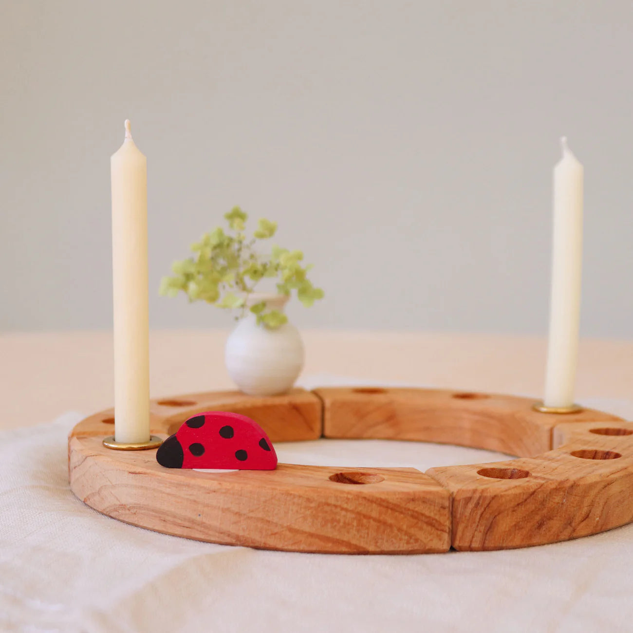 Grimms Geburtstagsring und Jahreszeitenring aus Holz mit Marienkäfer-Stecker im Vordergrund kombiniert mit Kerzen und Blumenvase im natürlichen Lifestyle-Look bei Burgfrollein