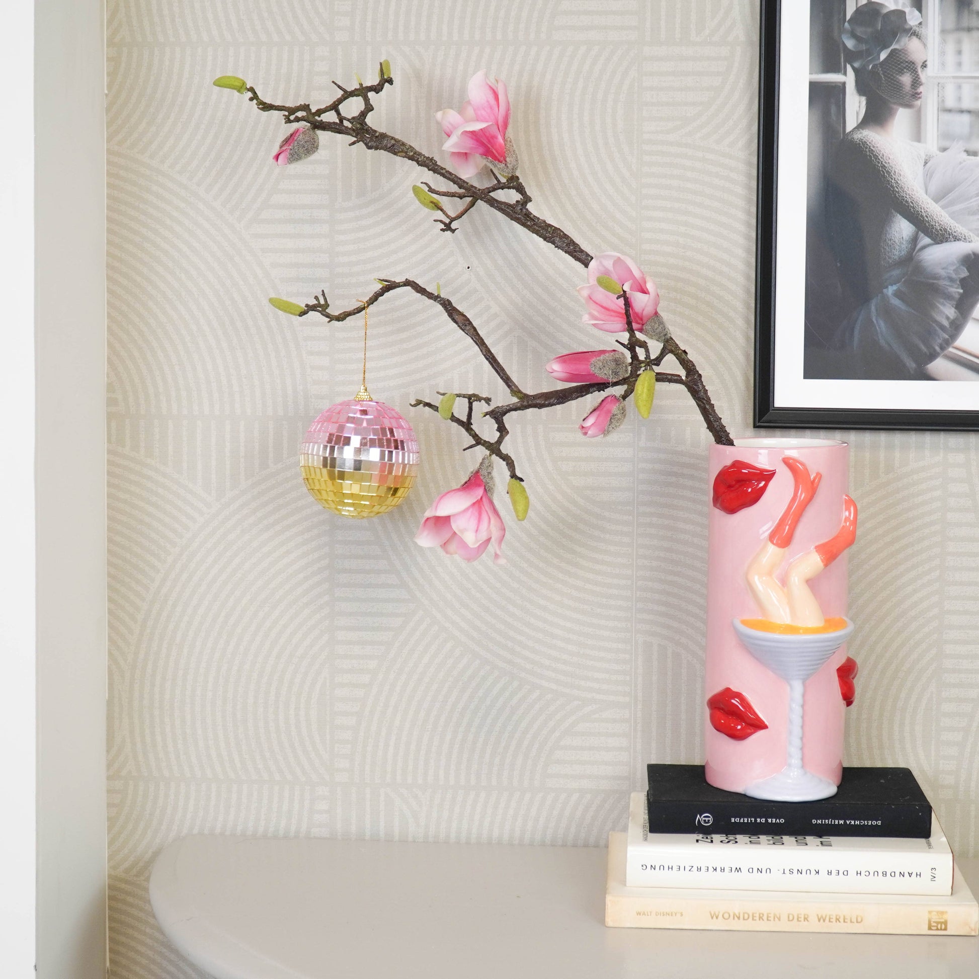 Discokugel für gute Laune von House Vitamin, 10 cm, in Rosa- und Goldtönen hängend an einem Magnolienzweig im stilvollen Wohnzimmer-Setting mit Büchern und Wandbild – funkelnde Wohnungsdeko und stimmungsvolle Geschenkidee