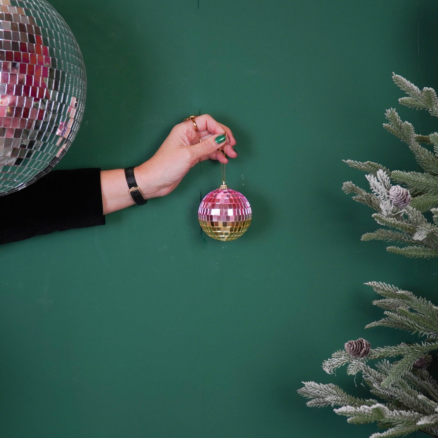 Discokugel für gute Laune von House Vitamin, 8 cm, in Rosa- und Goldtönen an Schnur in der Hand gehalten neben großer silberner Discokugel und Tannenzweigen auf grünem Hintergrund – funkelnde Weihnachtsdeko und stimmungsvolle Geschenkidee