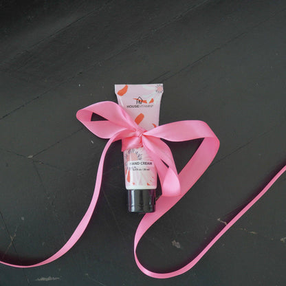 Kleine Tube Handcreme „Pfingstrosenblüte" von House Vitamin, 30 ml, mit großer gebundener rosa Schleife auf dunklem Holzuntergrund – florale Handpflege als festlich verpackte Geschenkidee