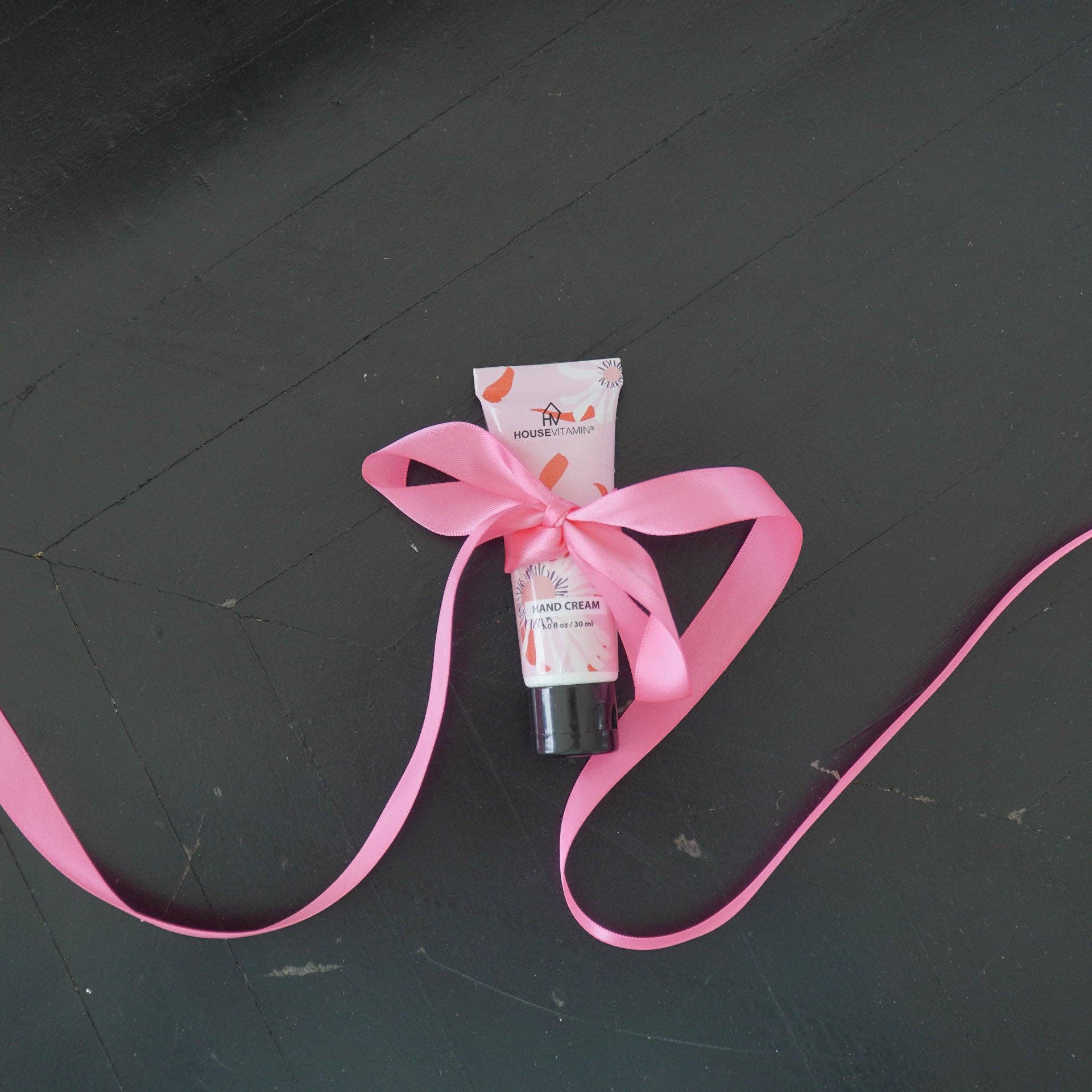 Kleine Tube Handcreme „Pfingstrosenblüte" von House Vitamin, 30 ml, mit rosa Geschenkschleife auf dunklem Holzuntergrund – pflegende Handpflege und liebevolle Geschenkidee
