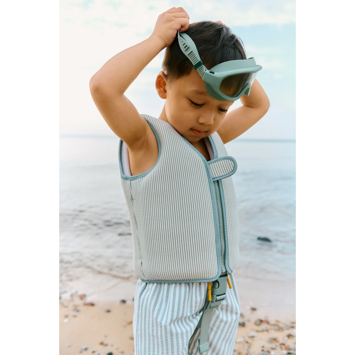 Kind am Strand mit Liewood Schwimmweste in Mint gestreift und passender Schwimmbrille im sommerlichen Lifestyle-Look bei Burgfrollein