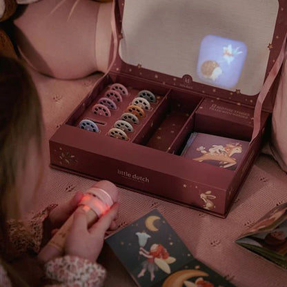 Little Dutch Geschichten-Taschenlampe aus der Fairy Garden Kollektion in Rosa projiziert das Bild eines Hasen in den Deckel der geöffneten rosa Geschenkbox, davor liegt ein Geschichtenheft