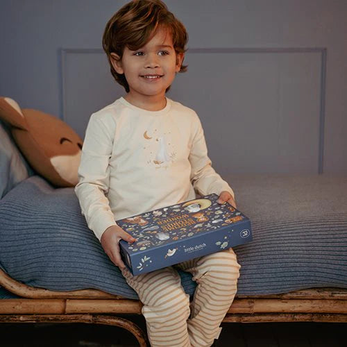 Kind sitzt auf Bett und hält die blaue Verpackung des Little Dutch Geschichten-Taschenlampen- und Projektor-Sets aus der Forest Friends Kollektion in den Händen