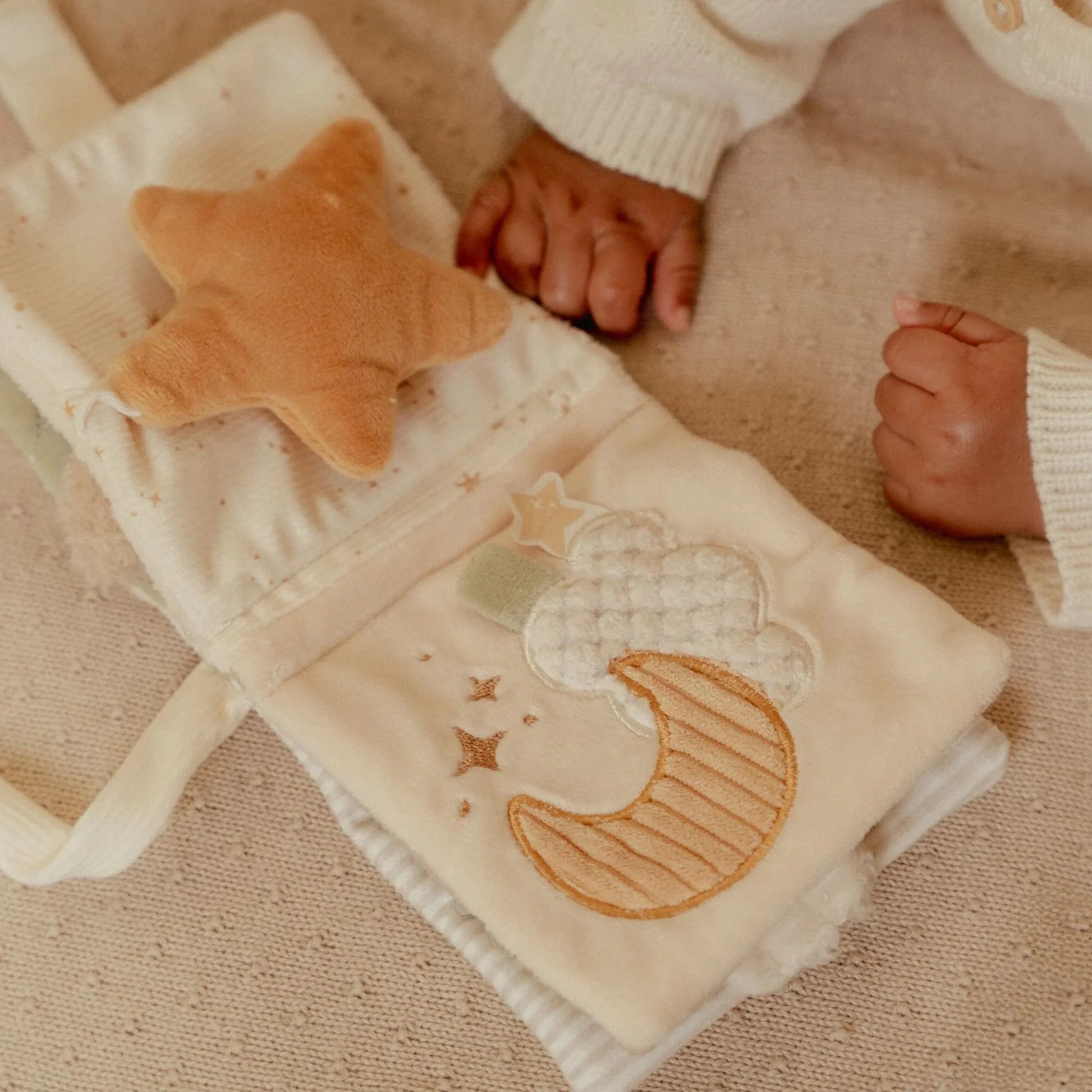 Zusammengefaltetes Little Dutch Buggybuch Newborn Naturals in Weiß mit Mond- und Sternstickerei, Baby greift danach – Babybuch für Kinderwagen und Maxi-Cosi bei Burgfrollein