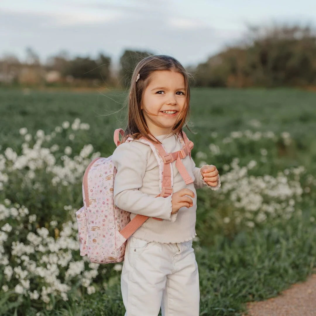 Mädchen trägt Little Dutch Kinderrucksack aus der Fairy Garden Kollektion in Rosa mit Brustgurt im Blumenfeld – ideal für jüngere Kinder, damit der Rucksack nicht von den Schultern rutscht
