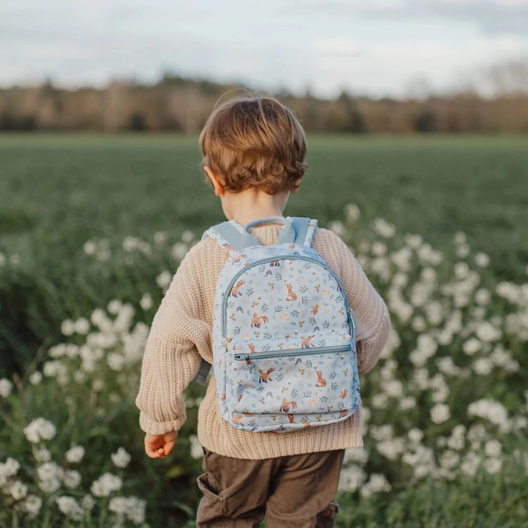Junge trägt Little Dutch Kinderrucksack aus der Forest Friends Kollektion in Hellblau mit kleinem Fuchs-Motiv und Pusteblumen-Print im Blumenfeld – ideal für Kindergarten und Kita