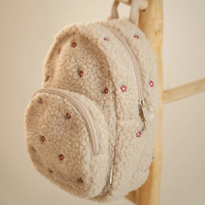 Little Dutch Teddy-Rucksack „Sand“ Detailansicht – Kinderrucksack aus weichem Teddyplüsch in Beige mit bestickten Blümchen und Reißverschluss, hängend an einer Holzleiter