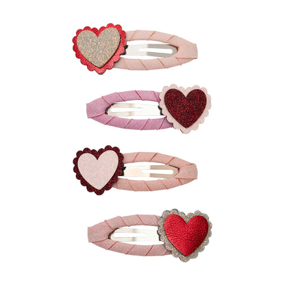 Gewellte Haarspangen mit Herz-Motiv von Mimi & Lula, 4er Set mit Herzen in Gold, Dunkelrot, Hellrosa und Rot mit gewelltem Rand auf rosa Stoffspangen, aufgereiht und freigestellt vor weißem Hintergrund – kinderfreundlicher Haarschmuck und liebevolle Geschenkidee