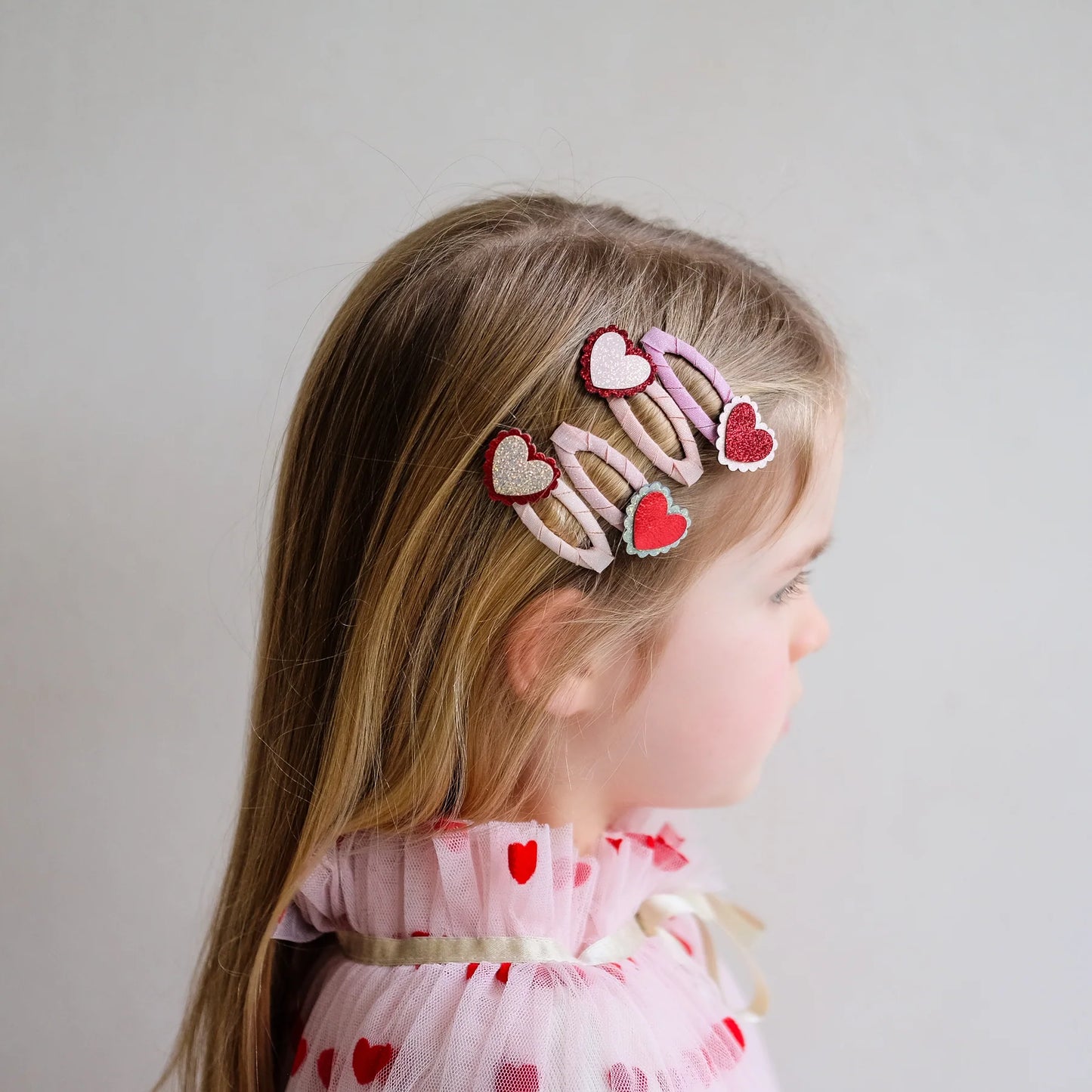 Gewellte Haarspangen mit Herz-Motiv von Mimi & Lula, 4er Set in Rosa-, Rot- und Cremetönen mit gestickten Herzen, getragen im Haar eines Kindes – kinderfreundlicher Haarschmuck und liebevolle Geschenkidee