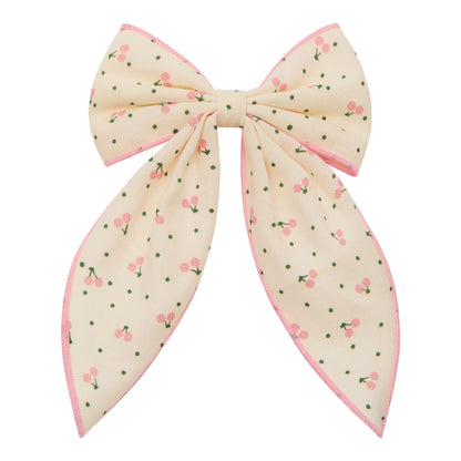 Haar-Schleife „Cherry" von Mimi & Lula, große cremefarbene Stoffschleife mit Kirsch-Print und rosa Rand, freigestellt vor weißem Hintergrund – kinderfreundlicher Haarschmuck und liebevolle Geschenkidee