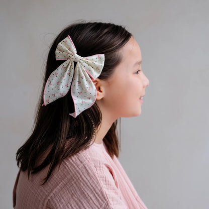 Haar-Schleife „Cherry" von Mimi & Lula, große weiße Stoffschleife mit Kirsch-Print und rosa Rand, getragen im Haar eines Kindes – kinderfreundlicher Haarschmuck und liebevolle Geschenkidee