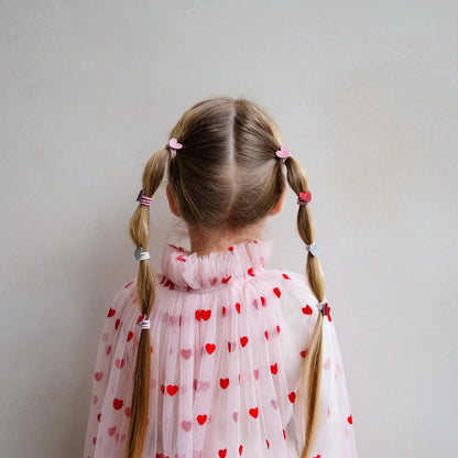 Kleine Haargummis mit Herz-Motiv von Mimi & Lula, 8er Set mit Stoff-Herzen in Gold-Glitzer, Rot, Rosa und Dunkelrot-Glitzer, getragen als Bubble-Zöpfe im Haar eines Kindes mit Herz-Cape von hinten – romantischer Haarschmuck für Kinder und liebevolle Geschenkidee