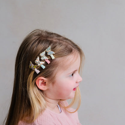 Kleine Schmetterling-Haarspangen von Mimi & Lula, 8er-Set in floralen Pastelltönen wie Rosa, Gelb, Hellblau und Creme mit Schmetterlings-Motiven, getragen im Haar eines Kindes – kinderfreundlicher Haarschmuck und liebevolle Geschenkidee