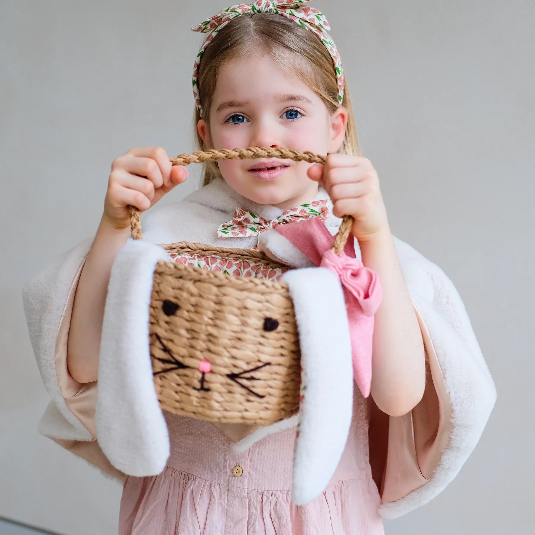 Mädchen hält Hasen-Osterkörbchen von Mimi & Lula mit Hasenohren und gestickter Hasenschnauze – geflochtener Osterkorb für Kinder mit rosa Schleife