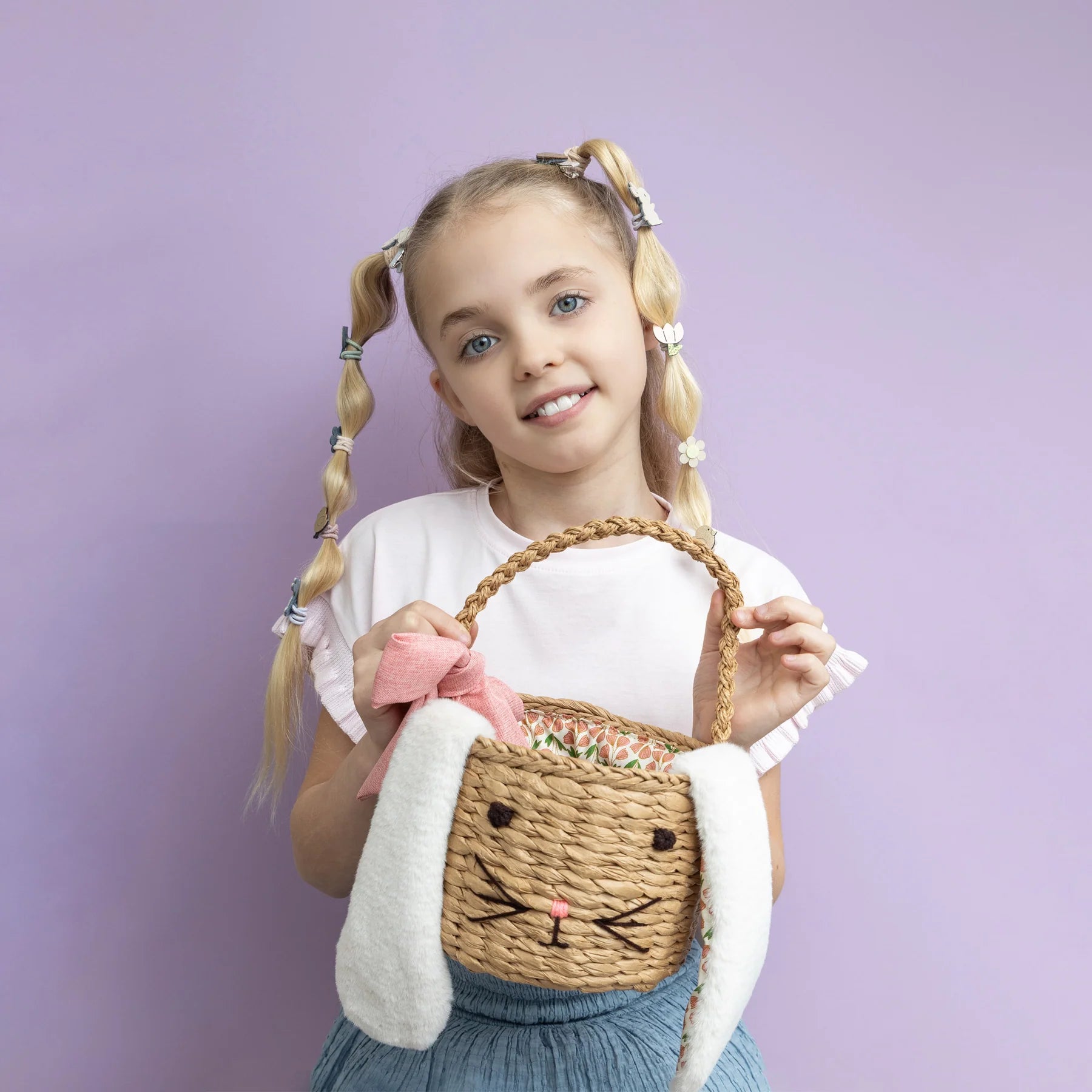 Mädchen mit Zöpfen hält Hasen-Osterkörbchen von Mimi & Lula mit Hasenohren und rosa Schleife – geflochtener Osterkorb für Kinder