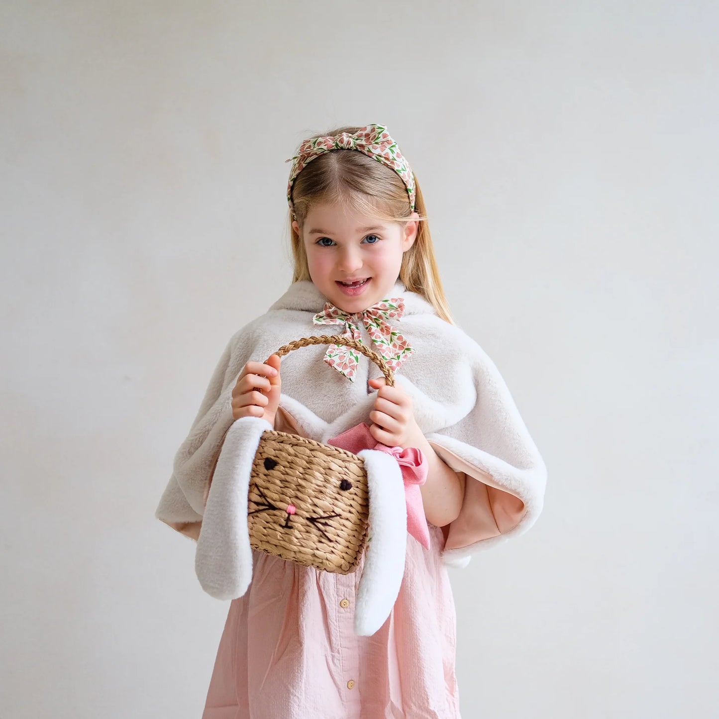 Mädchen trägt Hasen-Osterkörbchen von Mimi & Lula mit Hasenohren und rosa Schleife – stylisches Oster-Outfit für Kinder mit Bunny Cape und Tulpen-Haarreif