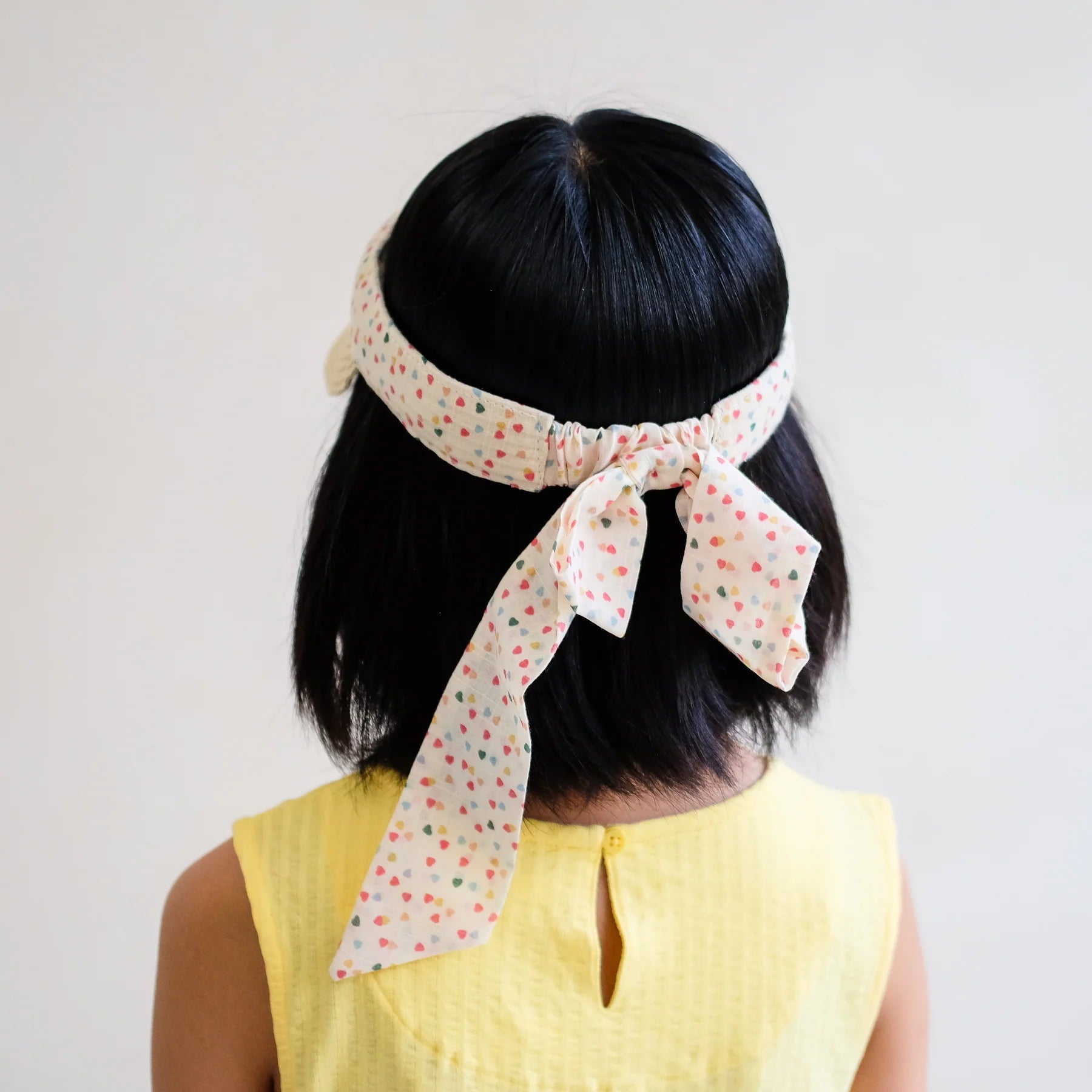 Rückansicht: Mädchen trägt sommerliche Sonnenvisier-Mütze Heart Print Visor mit Herz-Motiv und gebundener Schleife von Mimi & Lula – stylische Stroh-Sonnenblende für Kinder