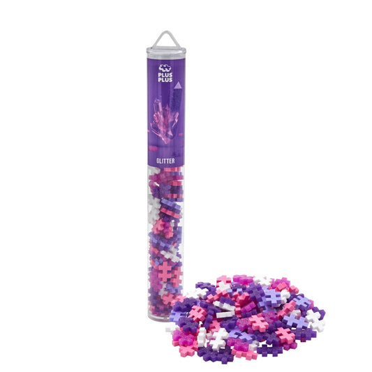 Plus-Plus Glitter Mix Tube mit 100 glitzernden Bausteinen in Lila, Pink und Weiß, davor Haufen ausgeschütteter Glitter-Steine