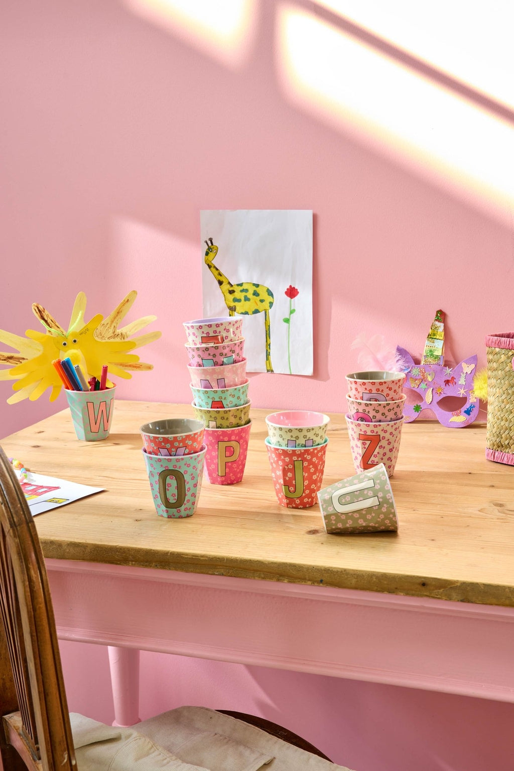RICE Buchstabenbecher Flowers auf einem Tisch vor rosa Wand – Geschenkidee zur Einschulung