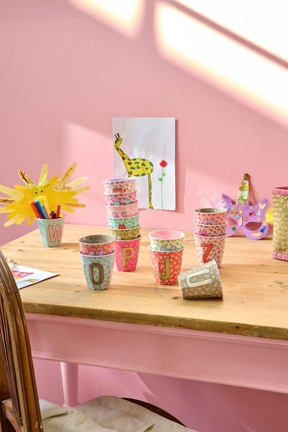 RICE Buchstabenbecher Flowers auf einem Tisch vor rosa Wand – Geschenkidee zur Einschulung