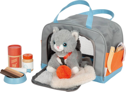 Spielszene aus dem Set „Katze mit Tasche und Pflegeset“ von Small Foot mit grauer Plüsch-Katze auf dem Plüsch-Kissen in der seitlich geöffneten Transporttasche, daneben Futternapf mit Leckerli-Dose und Spritze sowie Kamm und Spielmaus im orangen Seitenfach – nachhaltiges Rollenspielzeug zur Förderung der Fürsorge und Kreativität