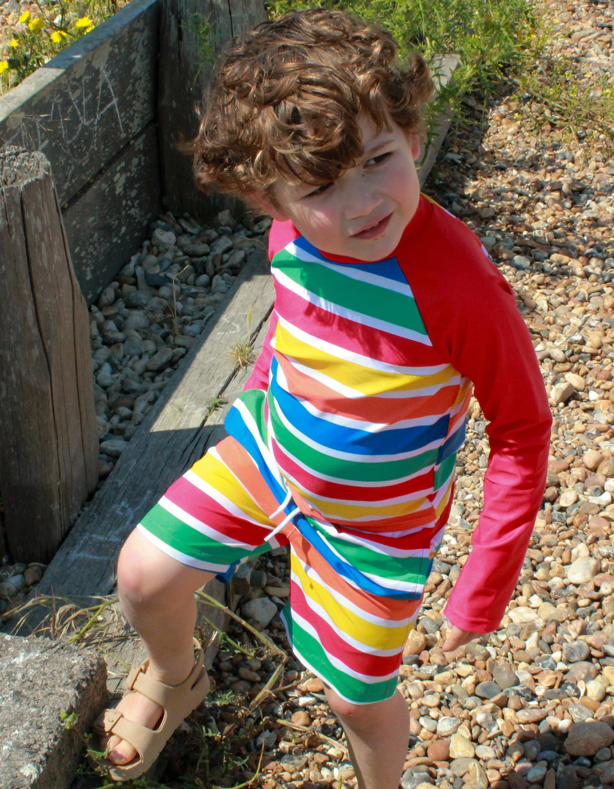 Kind trägt Toby Tiger Happy Stripes UV-Shirt und Badehose im Freien, bunte Streifen, UPF 50+