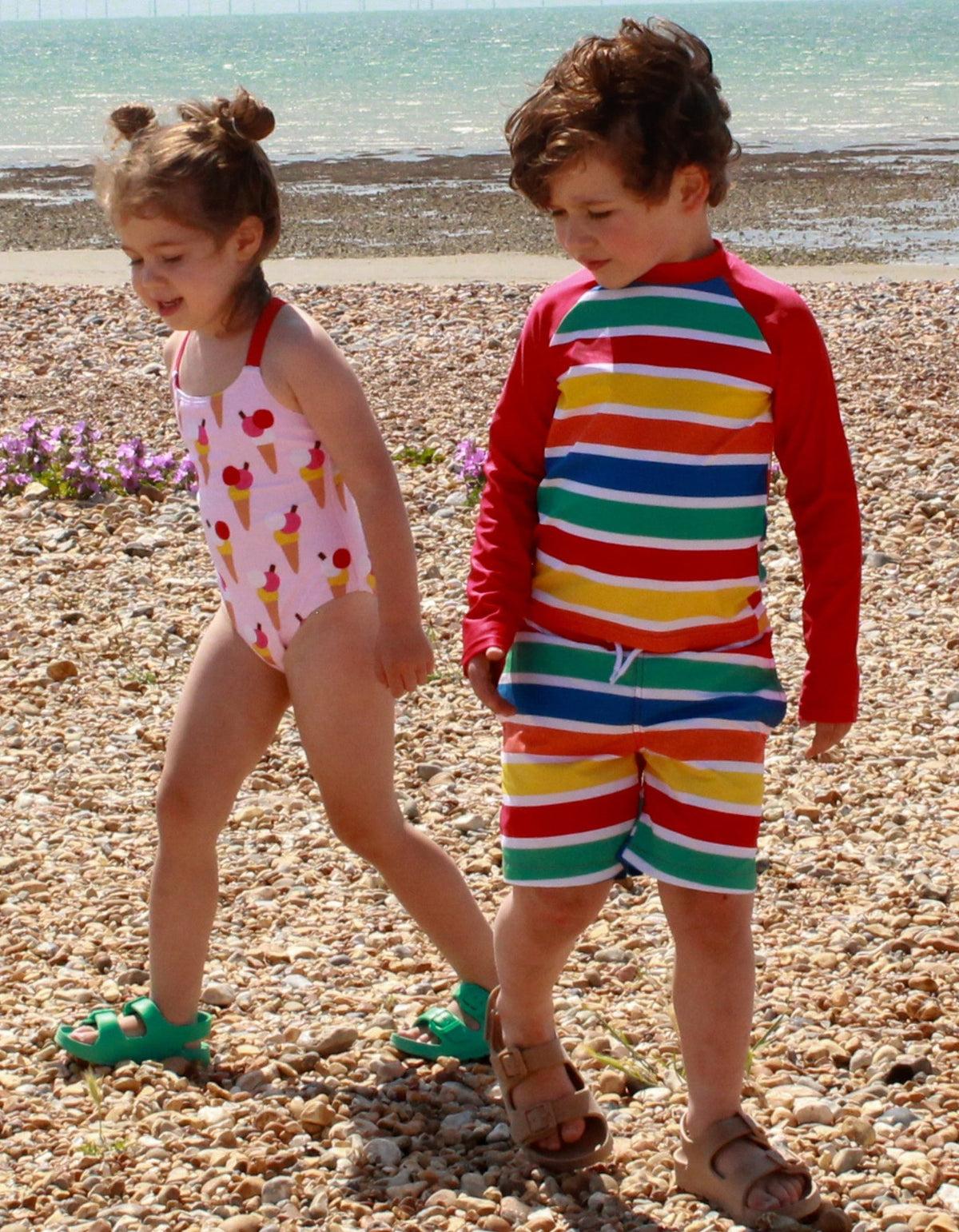 Kind trägt Toby Tiger Happy Stripes UV-Shirt und Badehose am Strand, bunte Streifen, UPF 50+