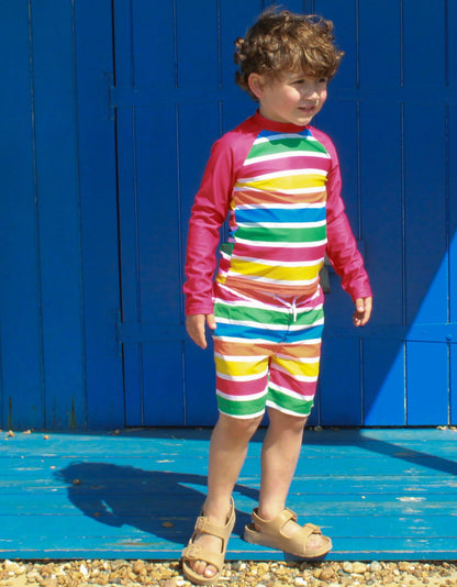 Kind trägt Toby Tiger Happy Stripes UV-Shirt und Badehose mit bunten Streifen, UPF 50+
