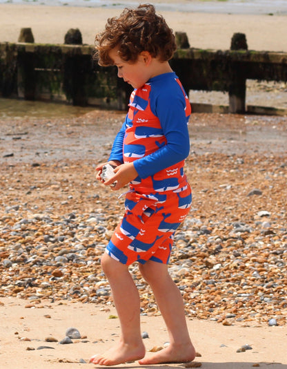 Kind am Strand im Toby Tiger UV-Schutz Shirt mit Wal- und Wellen-Print in Blau-Rot, UPF 50+ Badeshirt für Kinder
