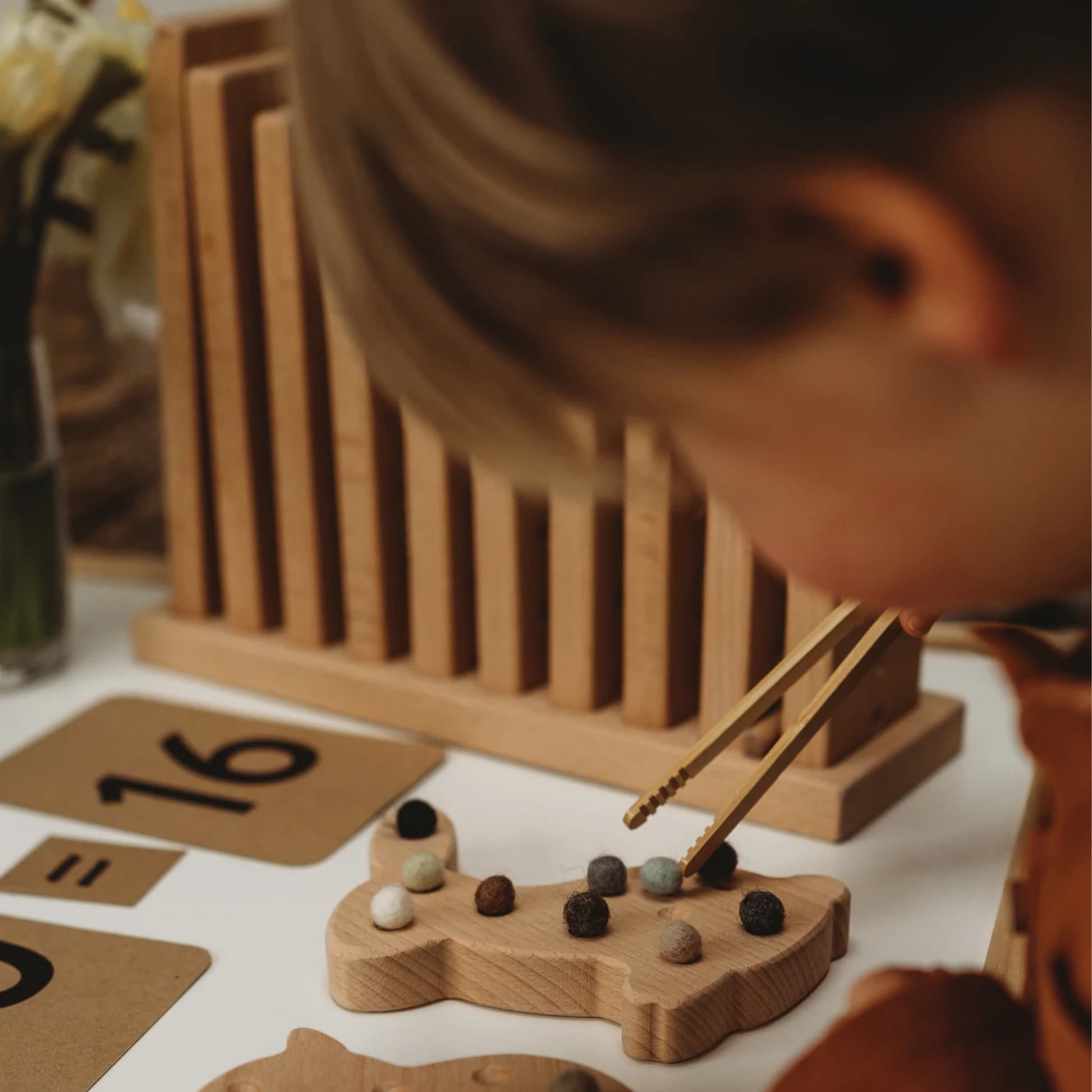 Kind übt mit Pinzette und Filzkugeln am Motorikbrett aus Holz in Hasenform – Montessori Feinmotorik für Kinder
